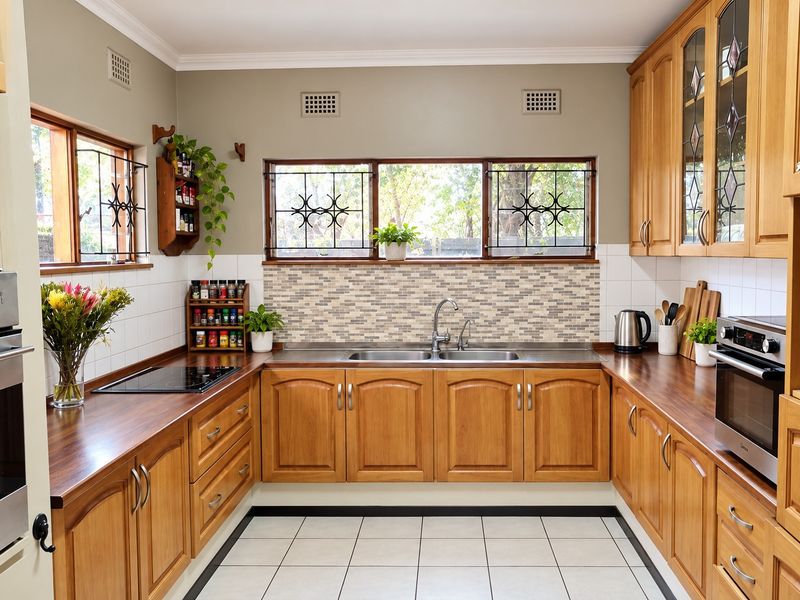 A well-maintained U-shaped kitchen featuring warm wooden cabinetry, dark laminate countertops, a double stainless steel sink, and integrated cooking appliances.
