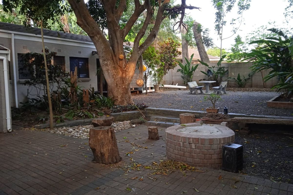 Rear garden area featuring a brick fire pit, paved patio space, and gravel landscaping with mature trees and boundary walls.
