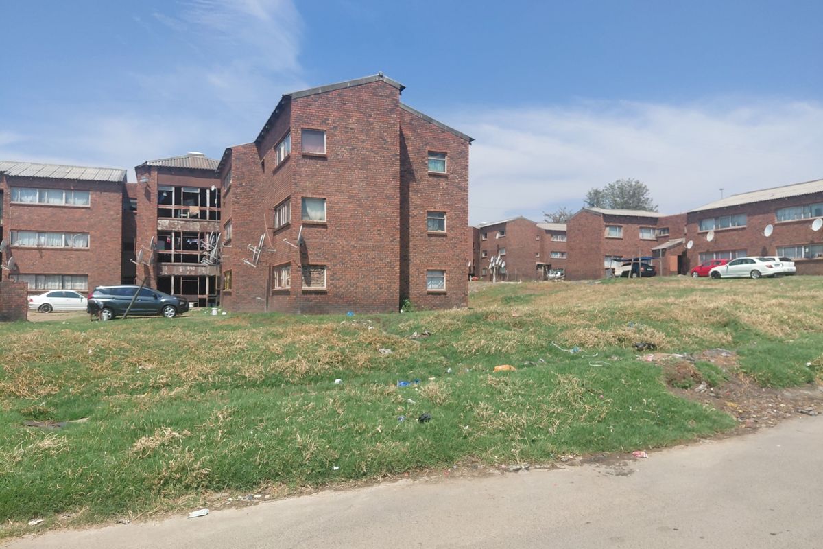 Exterior view of a multi-story brick residential complex with visible maintenance issues and missing window fixtures.