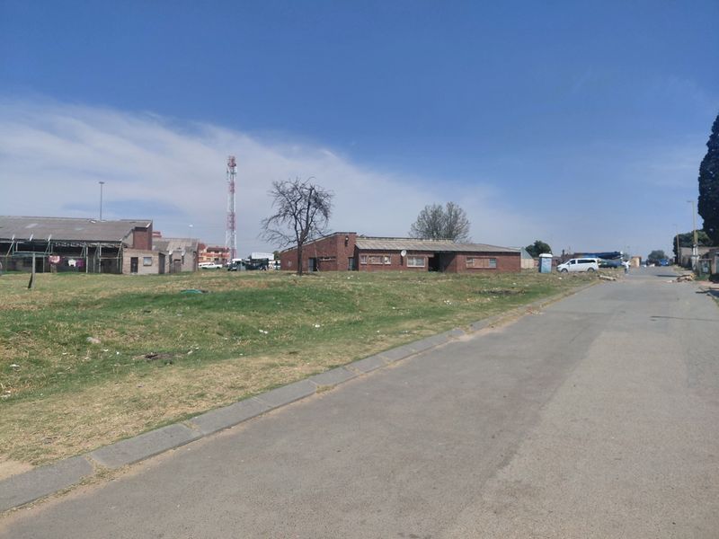 A street-level view of a residential area featuring brick-built structures, an asphalt road, and surrounding open land.