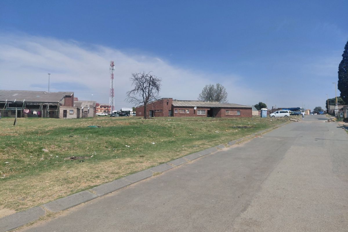 A street-level view of a residential area featuring brick-built structures, an asphalt road, and surrounding open land.