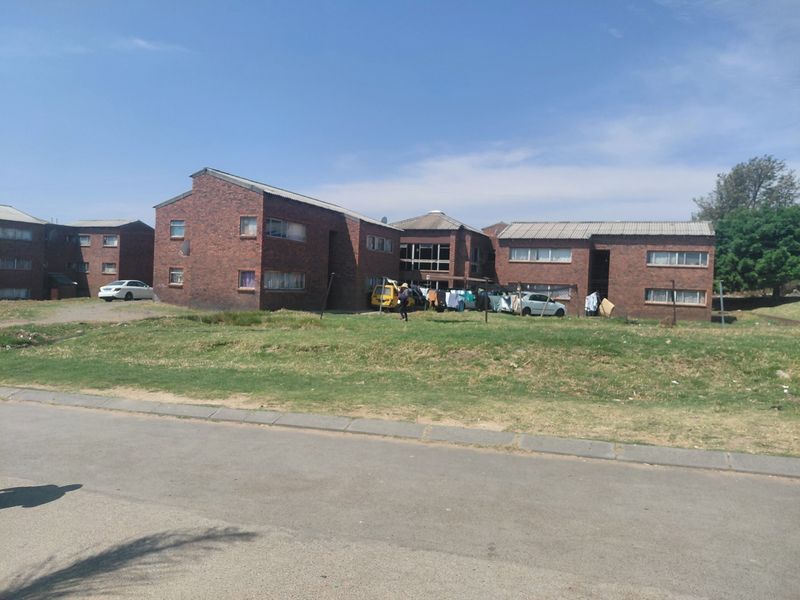 Exterior view of a multi-unit face brick residential complex with a pitched roof and surrounding grass area.