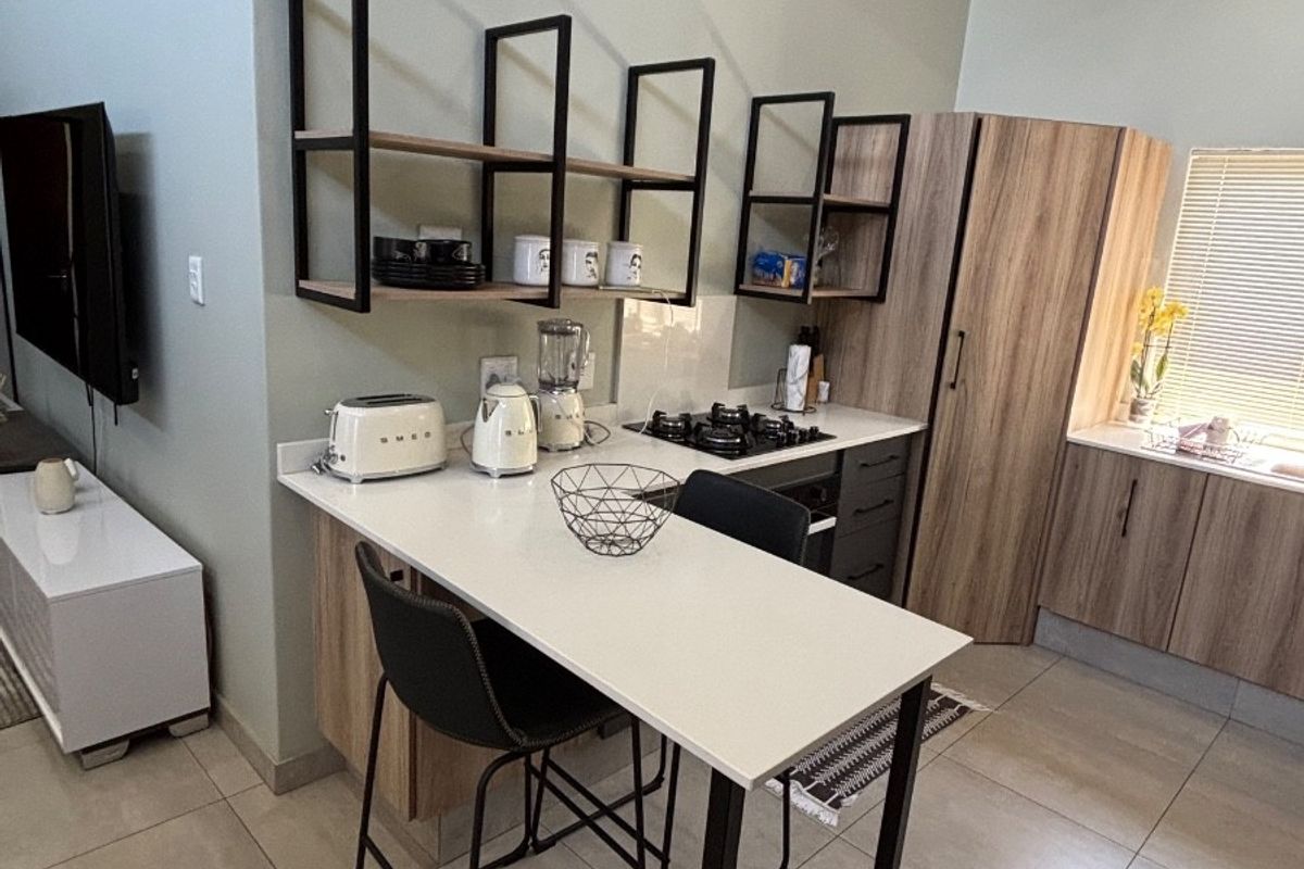 Modern kitchen featuring light wood cabinetry, stone countertops, gas hob, built-in oven, and striking exposed timber ceiling beams with tiled flooring throughout.