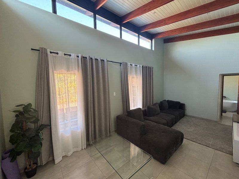 Spacious living room featuring high vaulted ceilings with exposed timber beams, clerestory windows for natural light, and neutral tiled flooring.