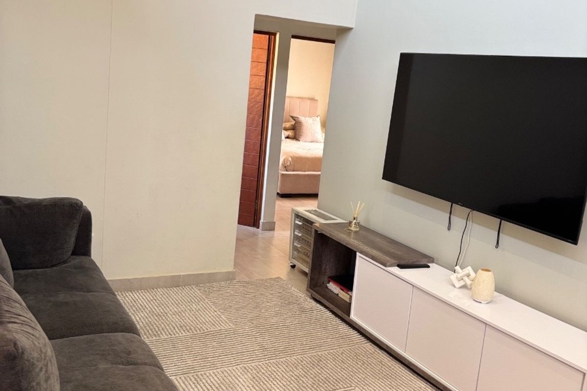 A bright living room featuring high ceilings, tiled flooring, and a direct view into an adjacent bedroom.