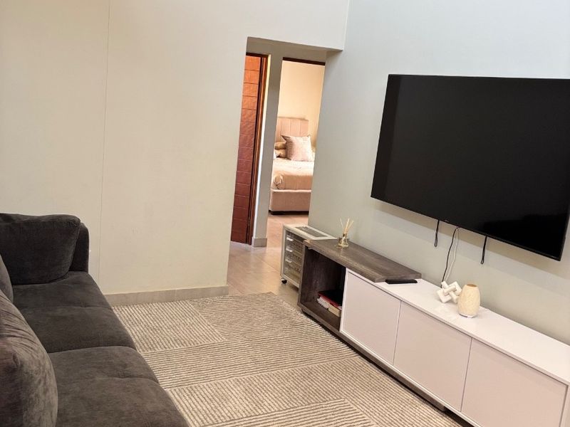 A bright living room featuring high ceilings, tiled flooring, and a direct view into an adjacent bedroom.