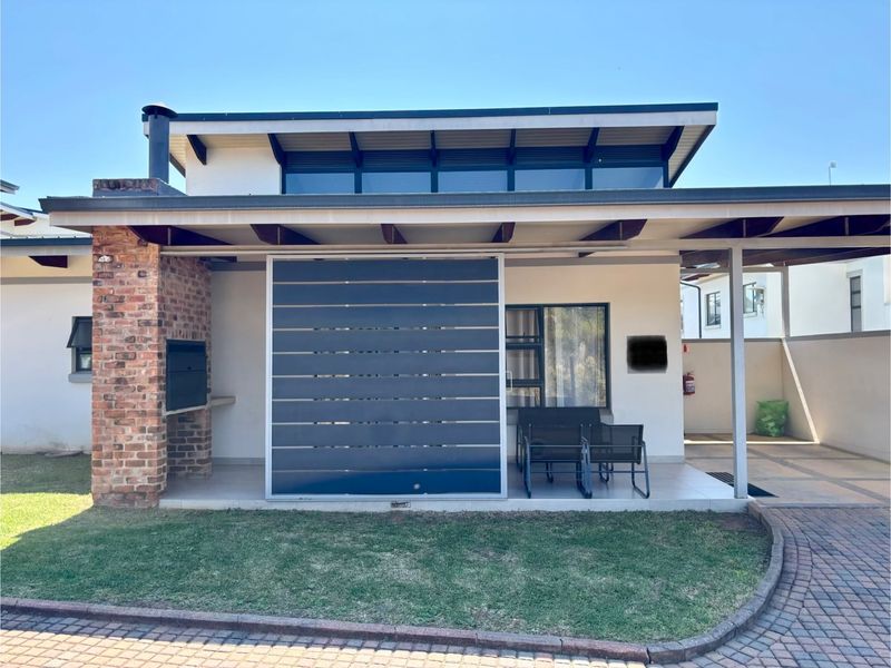 A covered patio area featuring a built-in brick fireplace, tiled flooring, and a privacy screen, overlooking a small garden space.