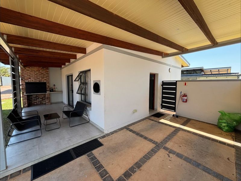Covered outdoor patio area featuring exposed timber beams, tiled flooring, and a built-in brick braai, perfect for outdoor entertaining.