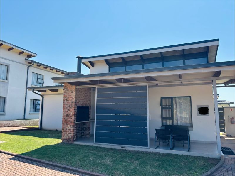 Covered patio area featuring a built-in brick braai, tiled flooring, and a modern privacy screen, overlooking a well-maintained garden space.