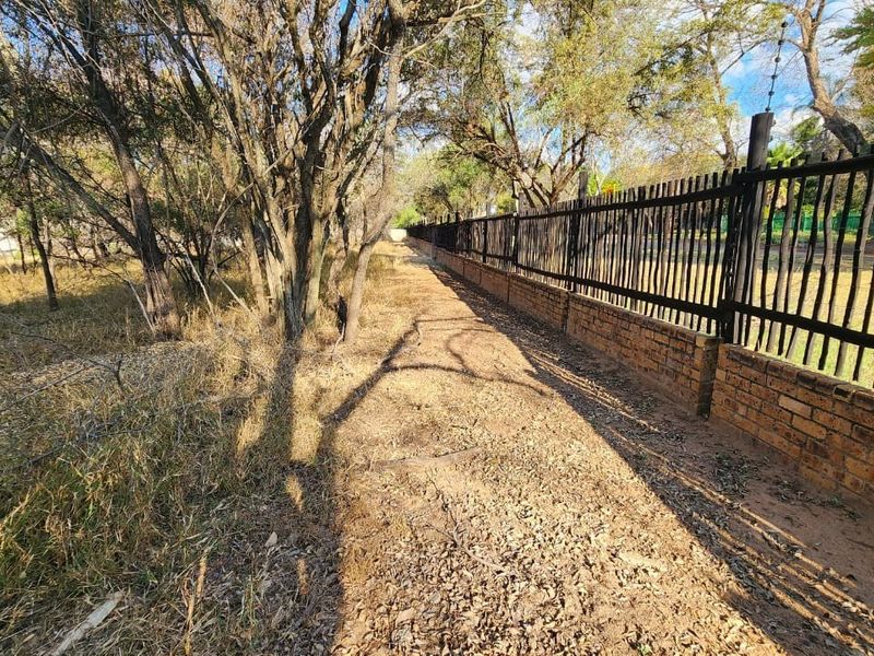 A view of the property boundary featuring a brick wall with steel security fencing and electric wire, bordering a natural wooded area.