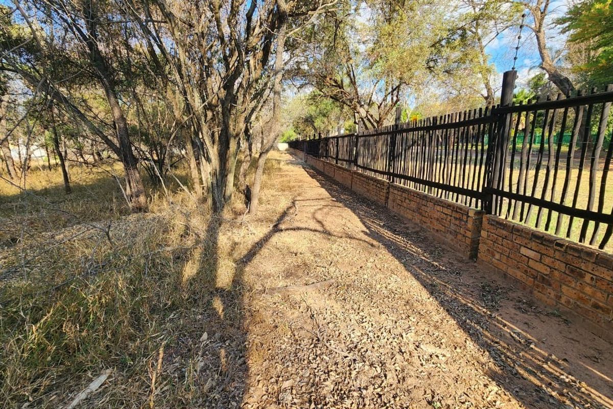 A view of the property boundary featuring a brick wall with steel security fencing and electric wire, bordering a natural wooded area.