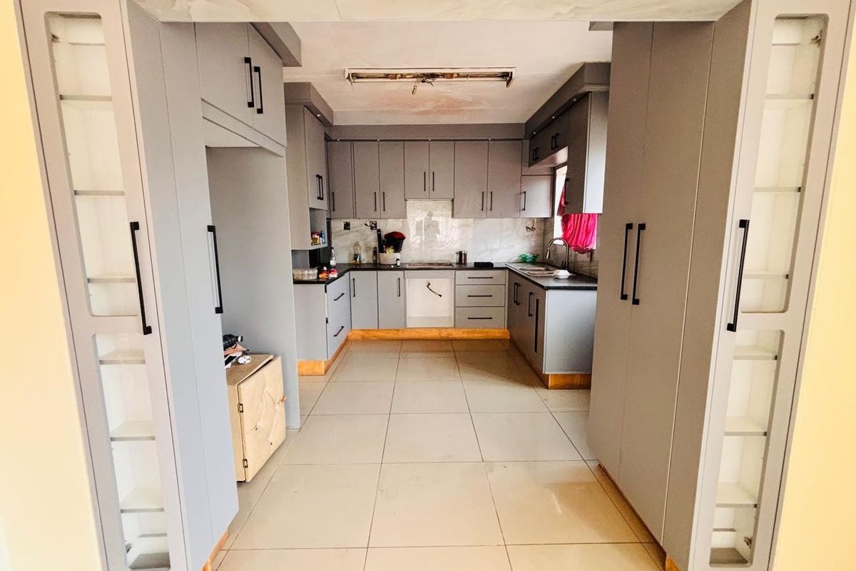A functional kitchen featuring grey built-in cabinetry, tiled flooring, and ample storage space, requiring minor ceiling repairs.