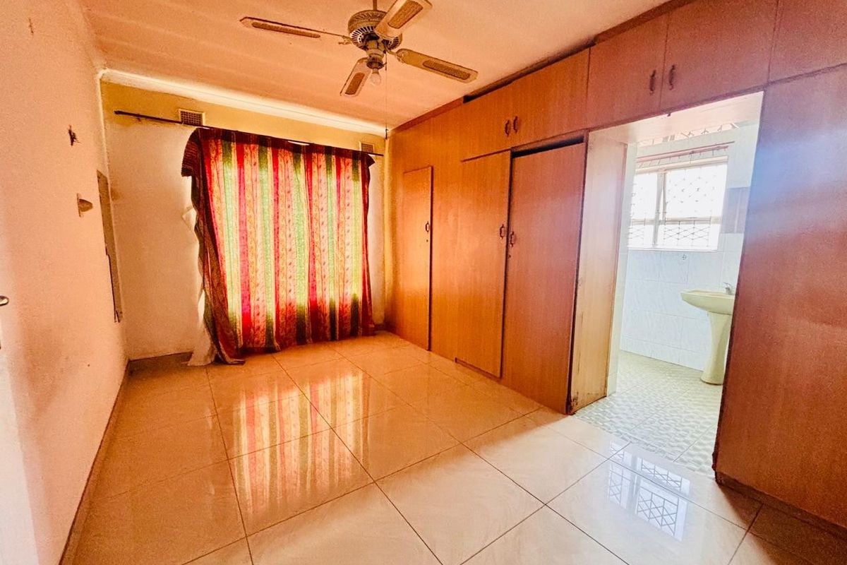 A vacant bedroom featuring built-in wooden cupboards, tiled flooring, and an attached en-suite area with a pedestal basin.