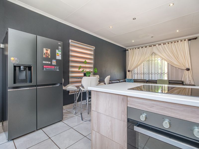 Modern open-plan kitchen and living area featuring a central island with built-in oven and hob, tiled flooring, and contemporary dark accent walls.