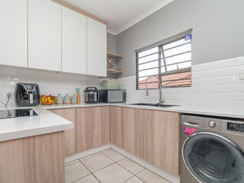 Modern kitchen featuring light wood-grain cabinetry, white subway tile backsplash, quartz countertops, and integrated laundry facilities.