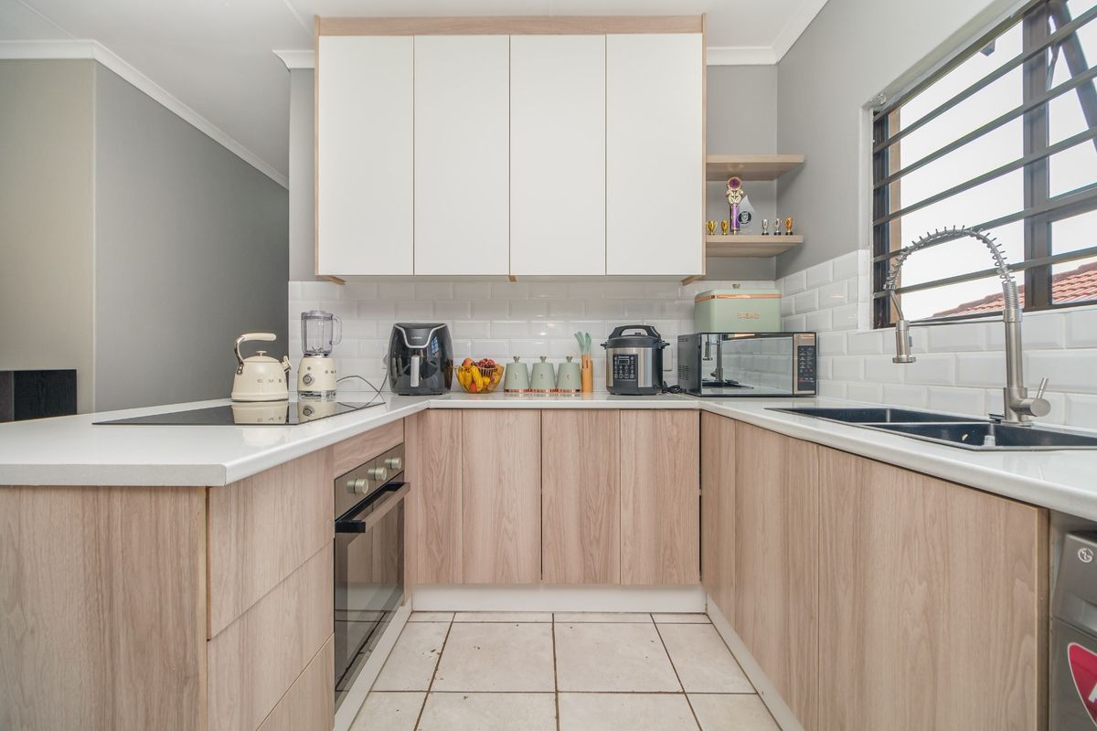 Modern U-shaped kitchen featuring light wood-tone cabinetry, white subway tile backsplash, quartz countertops, and integrated appliances.