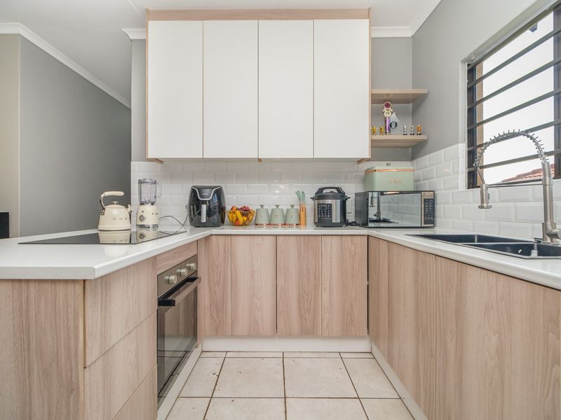 Modern U-shaped kitchen featuring light wood-tone cabinetry, white subway tile backsplash, quartz countertops, and integrated appliances.