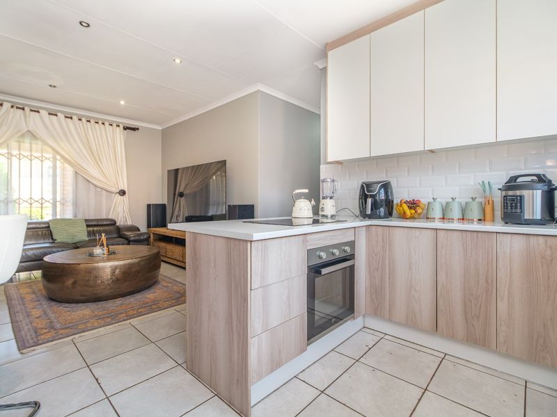 Modern open-plan kitchen and living area featuring light wood-finish cabinetry, subway tile backsplash, built-in oven, and tiled flooring throughout.