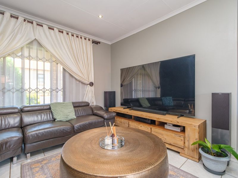 A well-maintained living room featuring tiled flooring, recessed downlighting, and a large window with security gate and curtain fixtures.