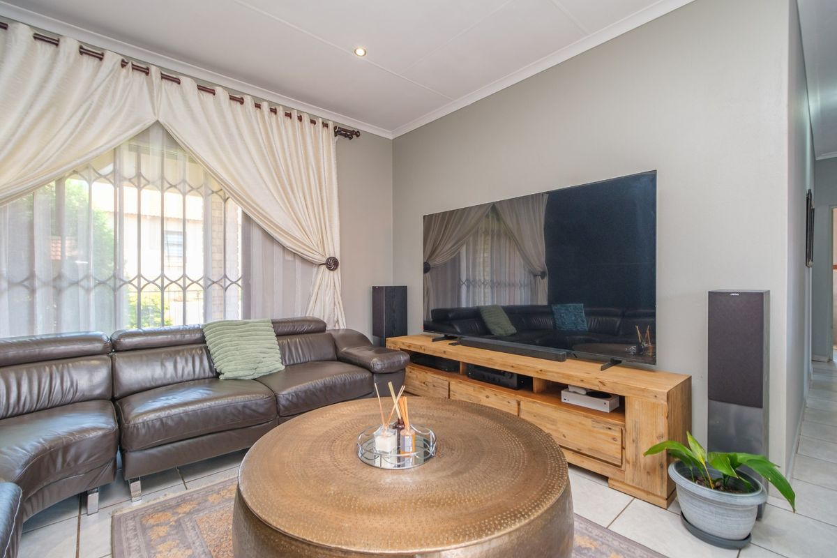 A well-maintained living room featuring tiled flooring, recessed downlighting, and a large window with security gate and curtain fixtures.