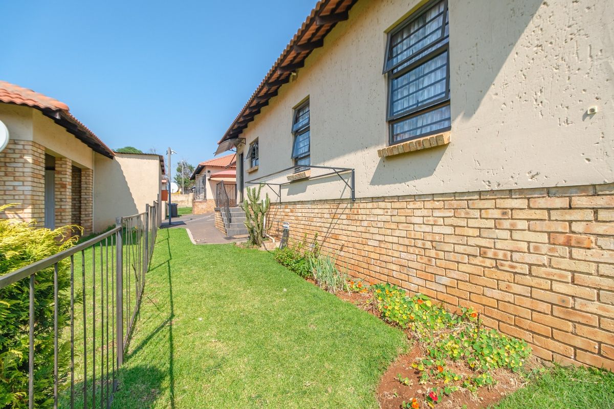 A view of the rear exterior of the house featuring a brick base, plastered walls, tiled roof, and a small garden area with metal fencing.