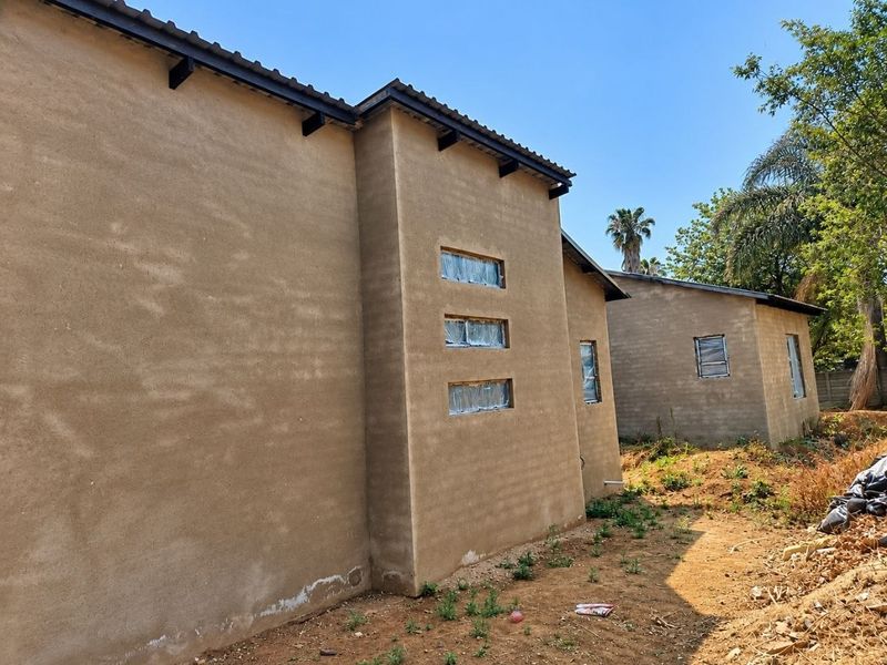 Rear view of a modern house under construction featuring plastered walls, tiled roofing, and horizontal windows with protective film.