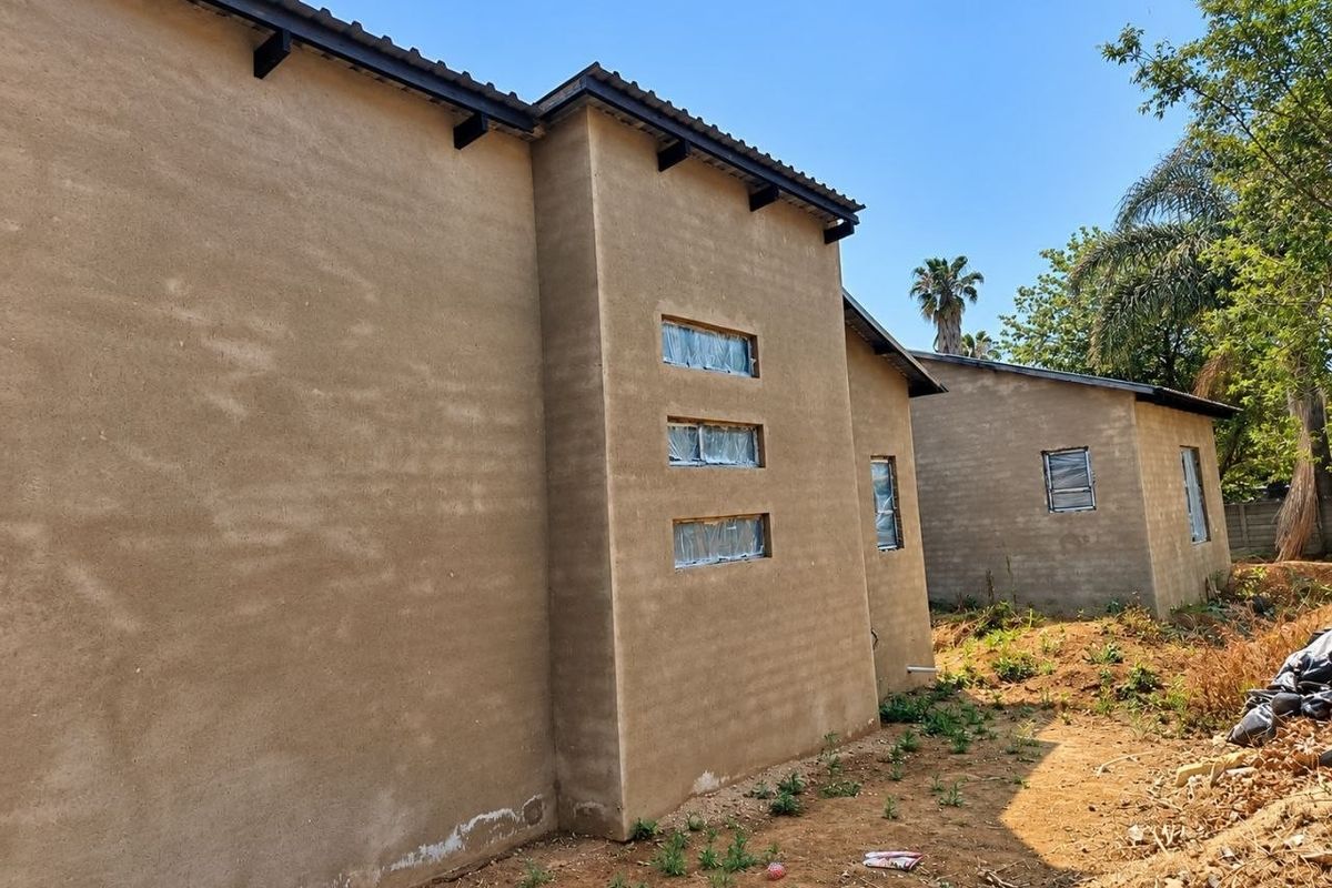 Rear view of a modern house under construction featuring plastered walls, tiled roofing, and horizontal windows with protective film.