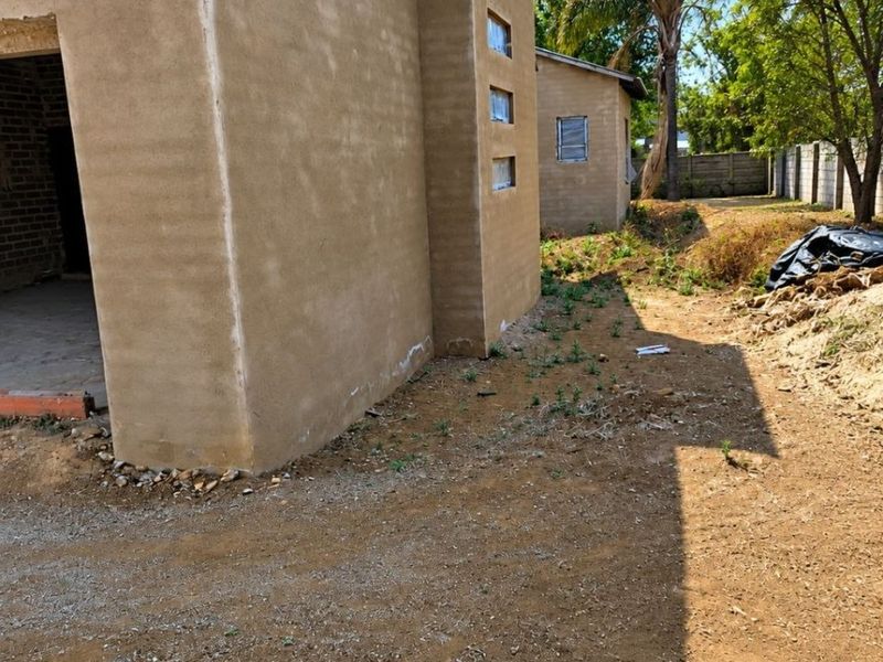Rear view of a property under construction featuring plastered walls, corrugated metal roofing, and unfinished surrounding grounds.