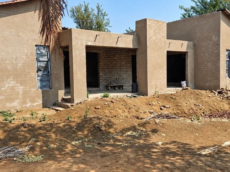 Rear view of a house under construction featuring plastered walls, aluminium window frames, and a covered patio area.
