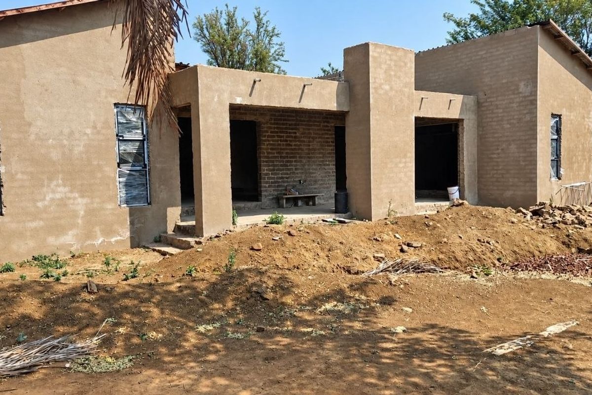 Rear view of a house under construction featuring plastered walls, aluminium window frames, and a covered patio area.
