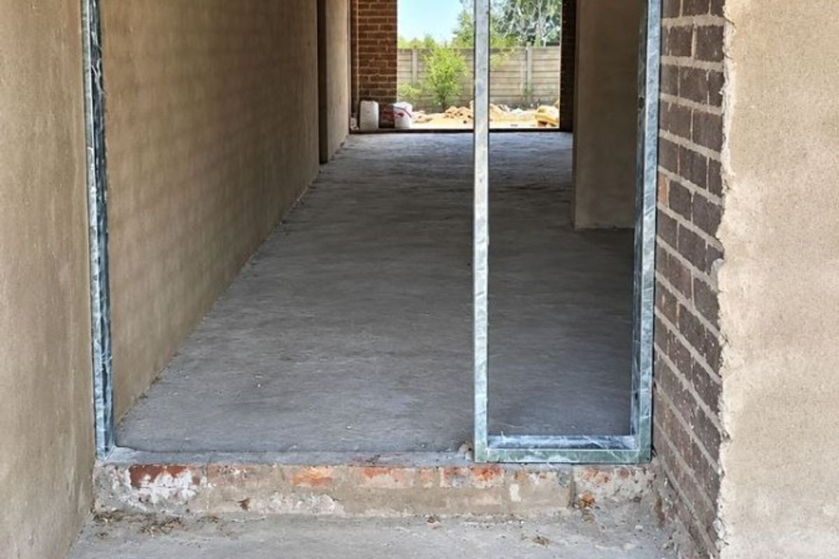 An unfinished hallway area under construction, featuring exposed brick walls, concrete flooring, and visible roof trusses, awaiting final interior finishes.