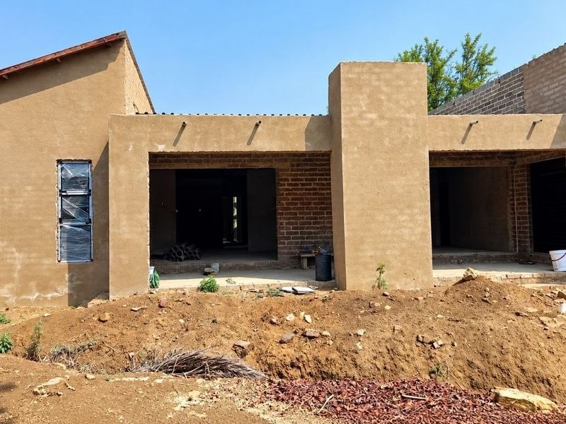 Rear view of a house under construction featuring plastered and exposed brick walls, covered patio areas, and aluminium window frames.