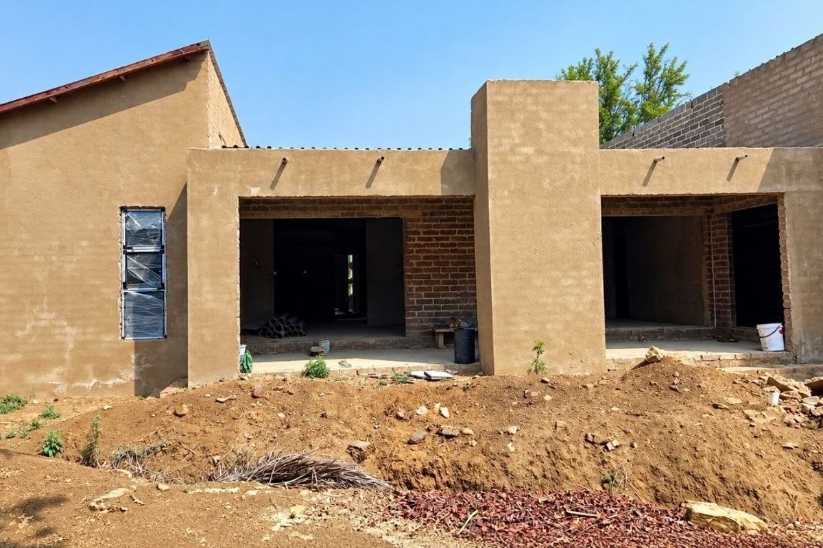 Rear view of a house under construction featuring plastered and exposed brick walls, covered patio areas, and aluminium window frames.
