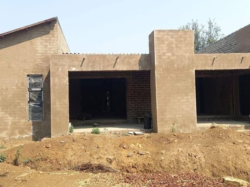 Rear view of a house under construction featuring plastered and exposed brick walls, aluminium windows, and an open covered patio area.