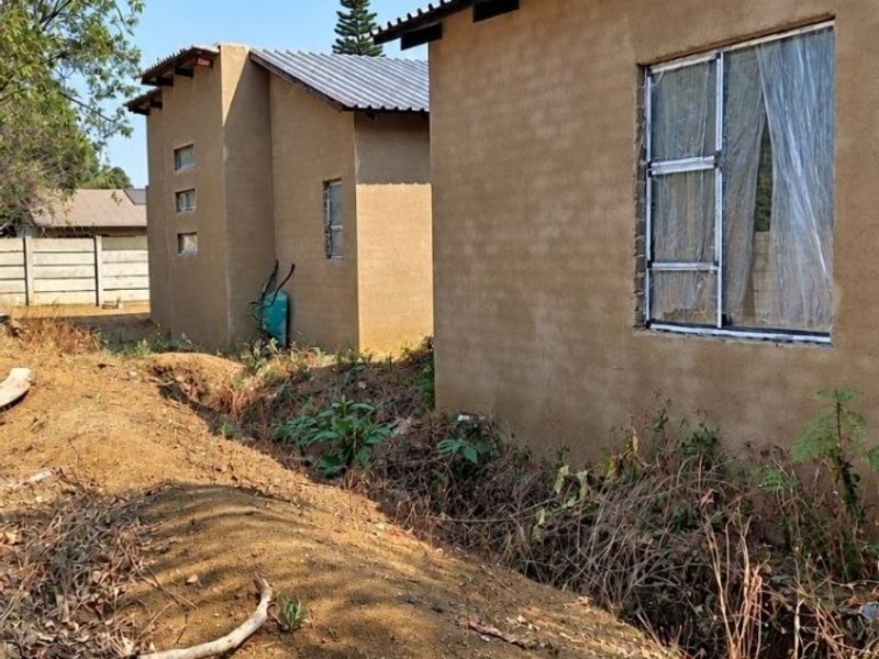 Exterior view of a residential property under construction, featuring plastered walls, metal roofing, and unfinished surrounding grounds.