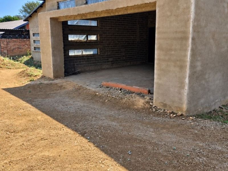 An exterior view of a house under construction, featuring exposed brickwork, cement plaster walls, and horizontal window openings.