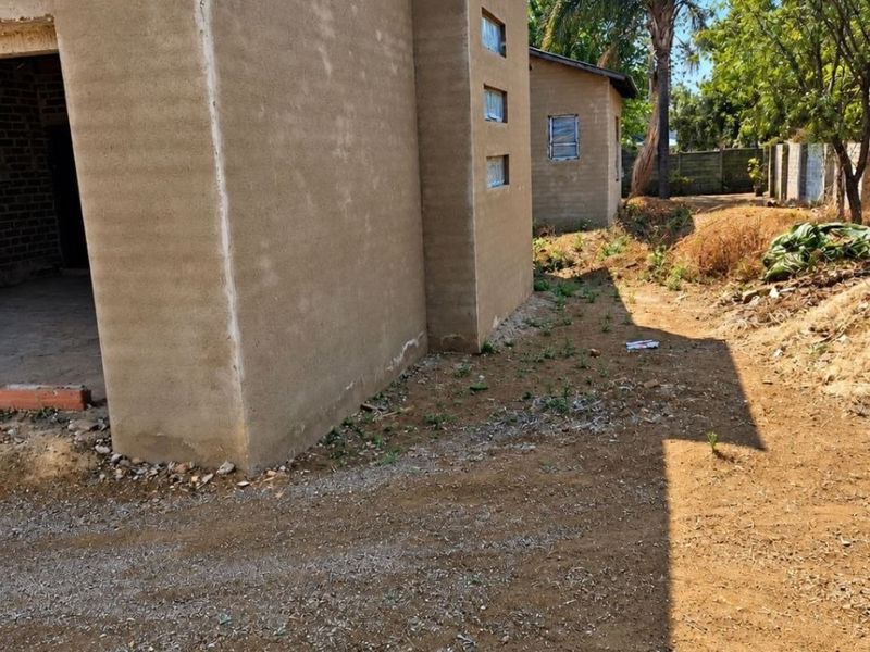 Rear view of a property under construction featuring plastered masonry walls, corrugated metal roofing, and an unlandscaped yard area.
