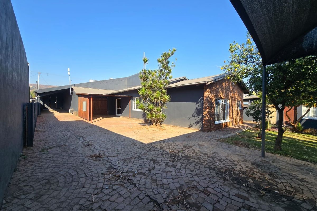 Rear exterior view of the house featuring a large cobblestone driveway, covered patio area, and a combination of brick and painted wall finishes.