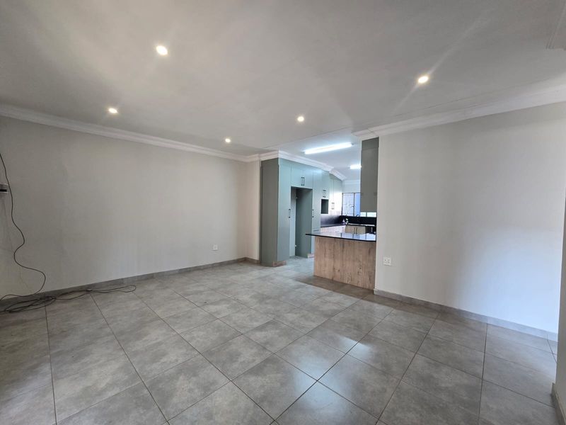 An open-plan living and kitchen area featuring modern tiled floors, recessed lighting, and a contemporary kitchen with a breakfast island.