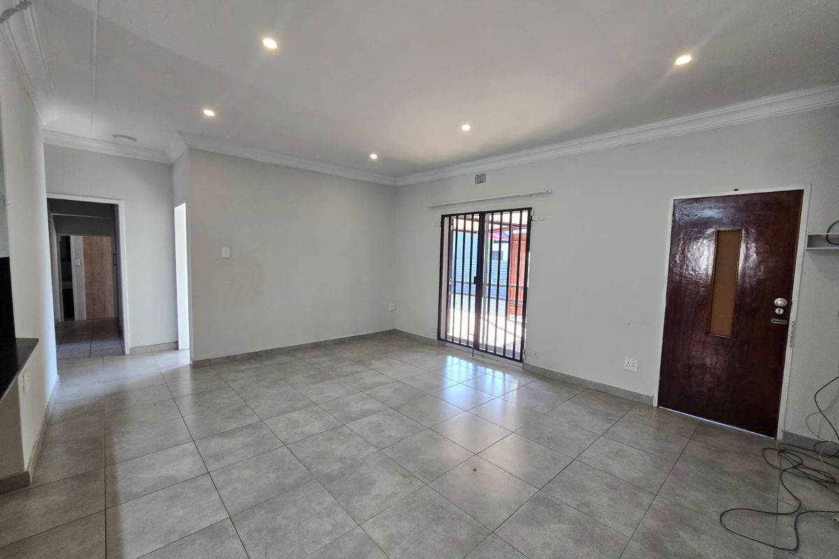 A spacious, empty living area featuring neutral tiled flooring, recessed downlighting, and a secure sliding door leading to the exterior.