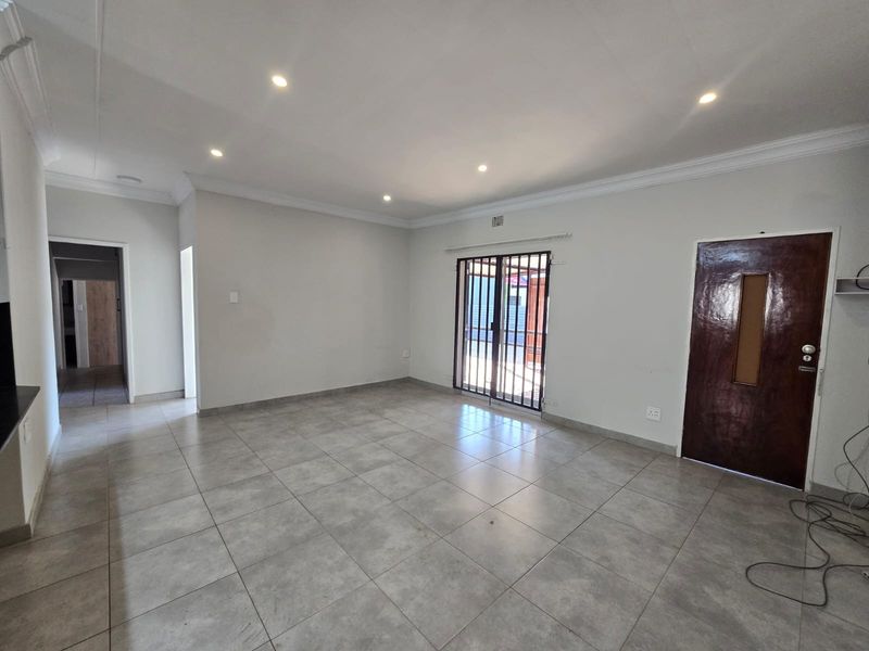 A spacious, empty living area featuring neutral tiled flooring, recessed downlighting, and a secure sliding door leading to the exterior.