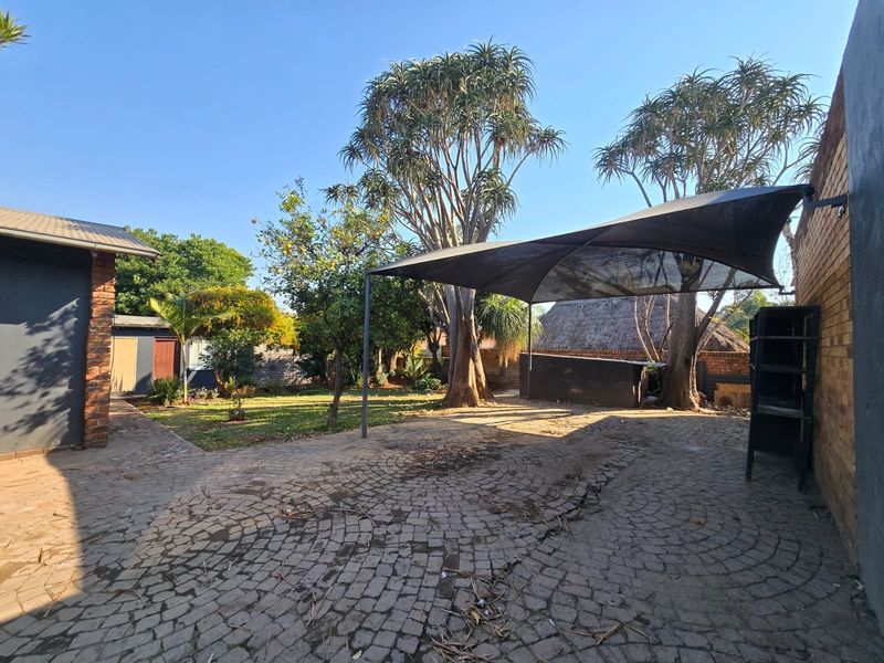 Rear garden area featuring cobblestone paving, a shade sail, and a built-in braai structure, offering a functional outdoor entertainment space.