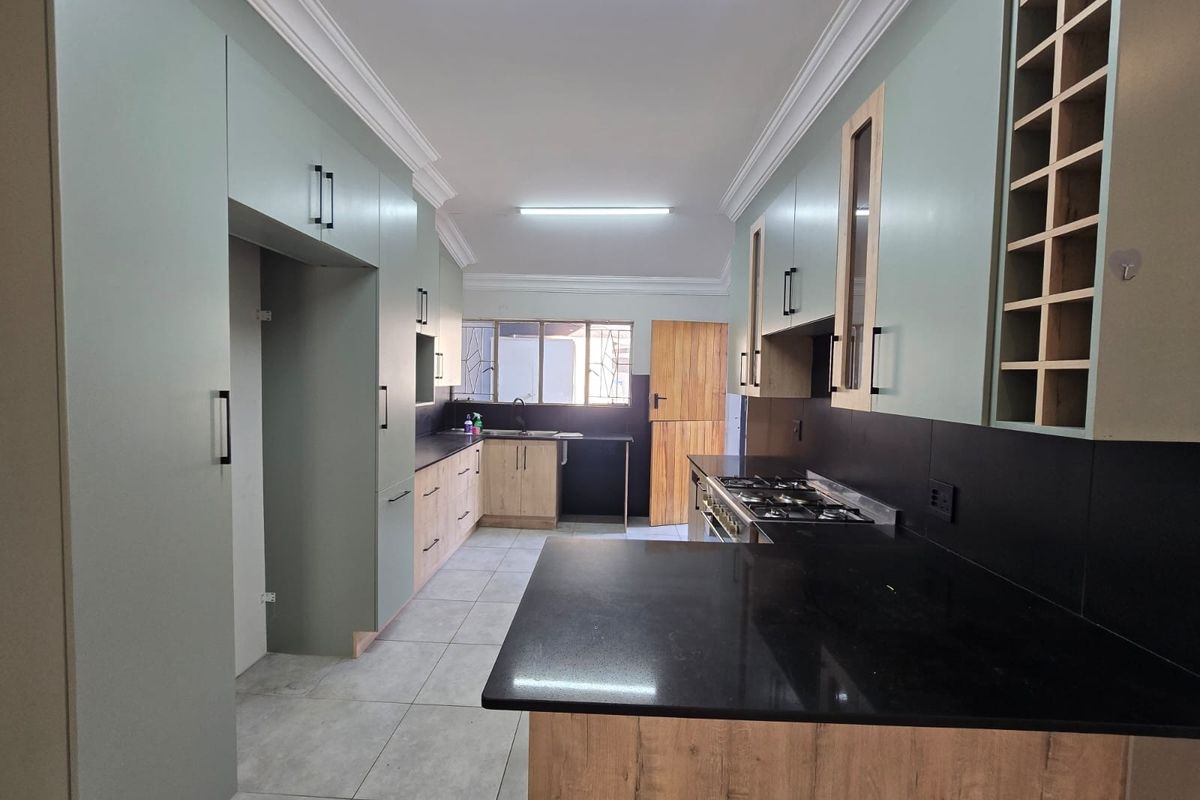Modern kitchen featuring sage green and wood-grain cabinetry, black stone countertops, a gas hob, and tiled flooring in a clean, well-maintained space.