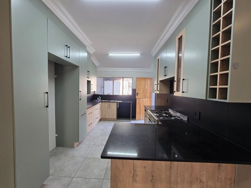 Modern kitchen featuring sage green and wood-grain cabinetry, black stone countertops, a gas hob, and tiled flooring in a clean, well-maintained space.