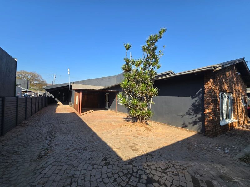 Exterior view of the property featuring a cobblestone driveway, covered carport, and a combination of brick and dark-painted wall finishes.