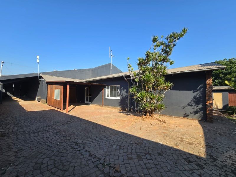 Rear exterior view of the property featuring a paved courtyard, covered patio area, and dark-painted exterior walls.