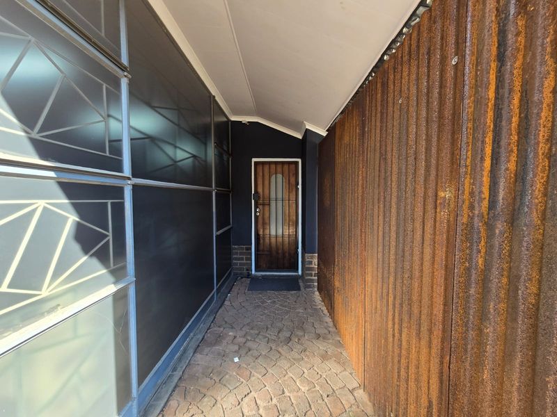 A covered entrance walkway featuring a timber front door, paved flooring, and distinctive corrugated metal wall cladding.