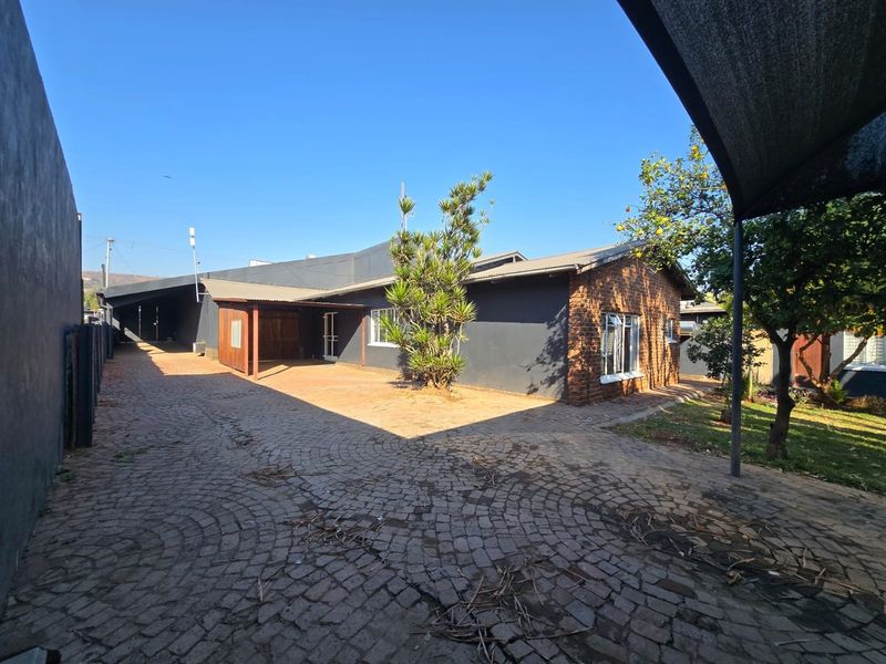 Rear exterior view of the house featuring a large cobblestone driveway, covered patio area, and a combination of brick and painted wall finishes.