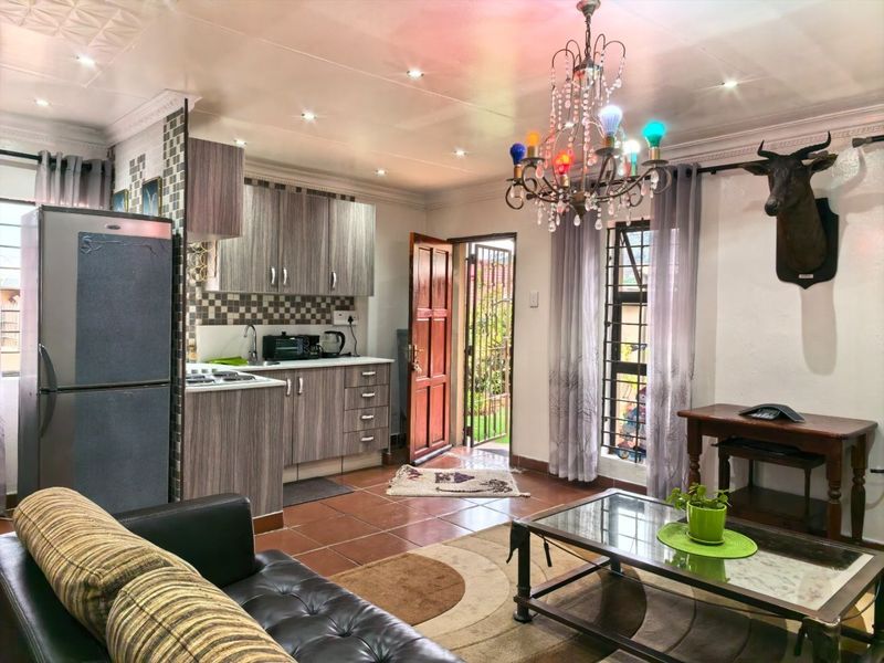 Open-plan living area featuring a compact kitchen with built-in cabinetry, tiled flooring, and direct access to the exterior through a security gate.