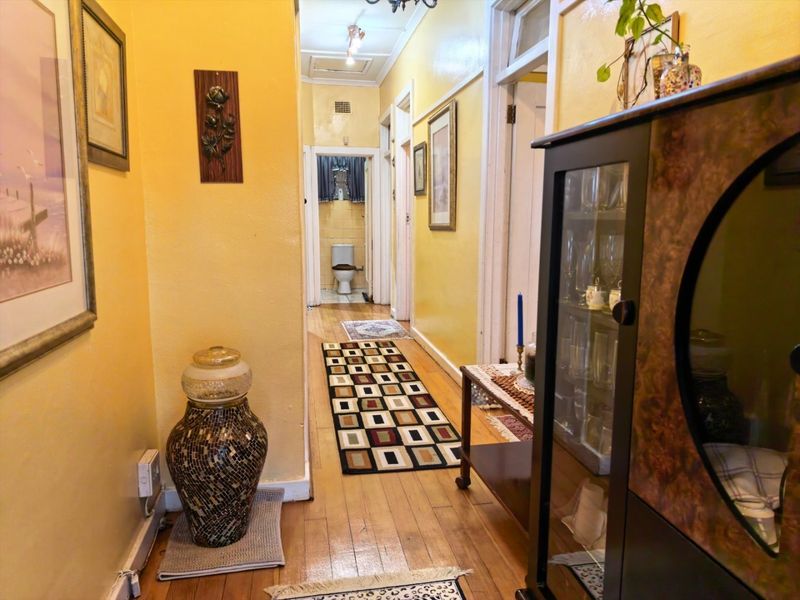 A traditional hallway featuring hardwood flooring and access to adjacent rooms, including a view toward a bathroom at the end of the corridor.